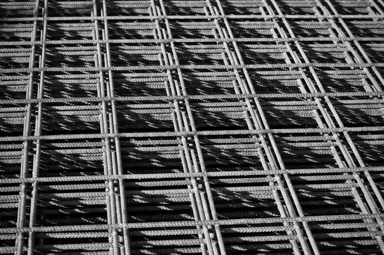 services-04 Close-up of a steel rebar grid creating a geometric pattern in black and white.